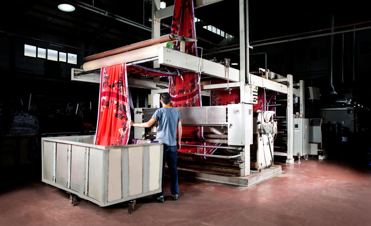 contact-img Worker operates machinery in a textile factory, overseeing fabric production.